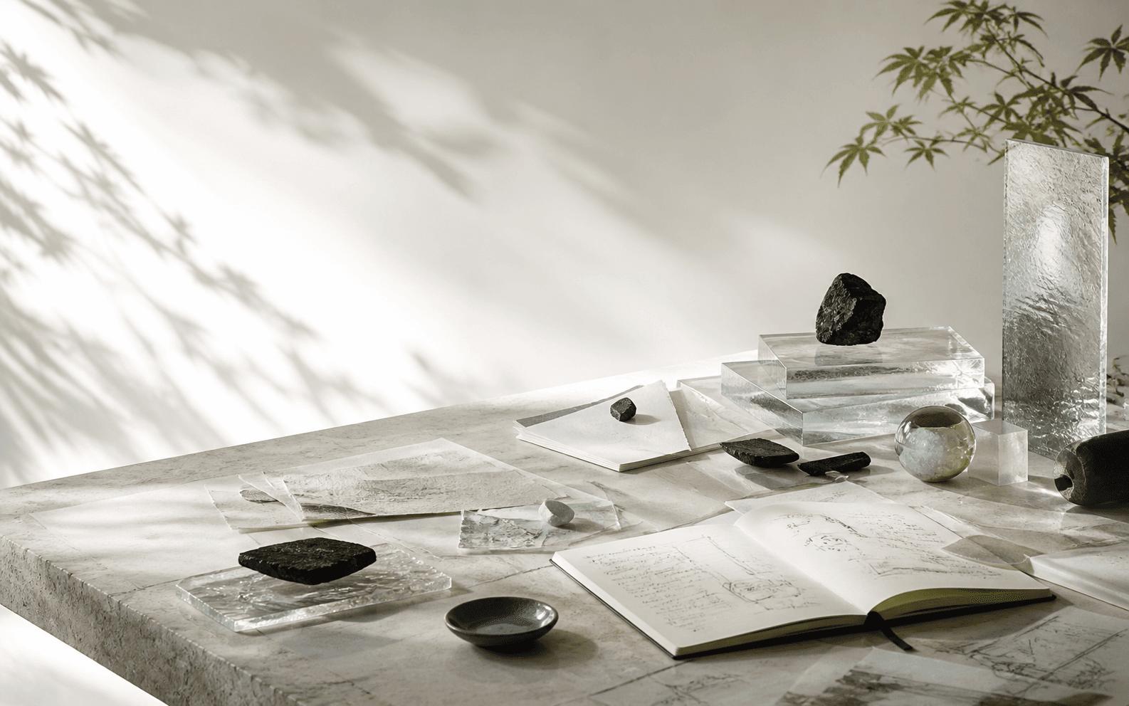 A daylight studio table with mineral glass, paper, and tools arranged for collaborative work